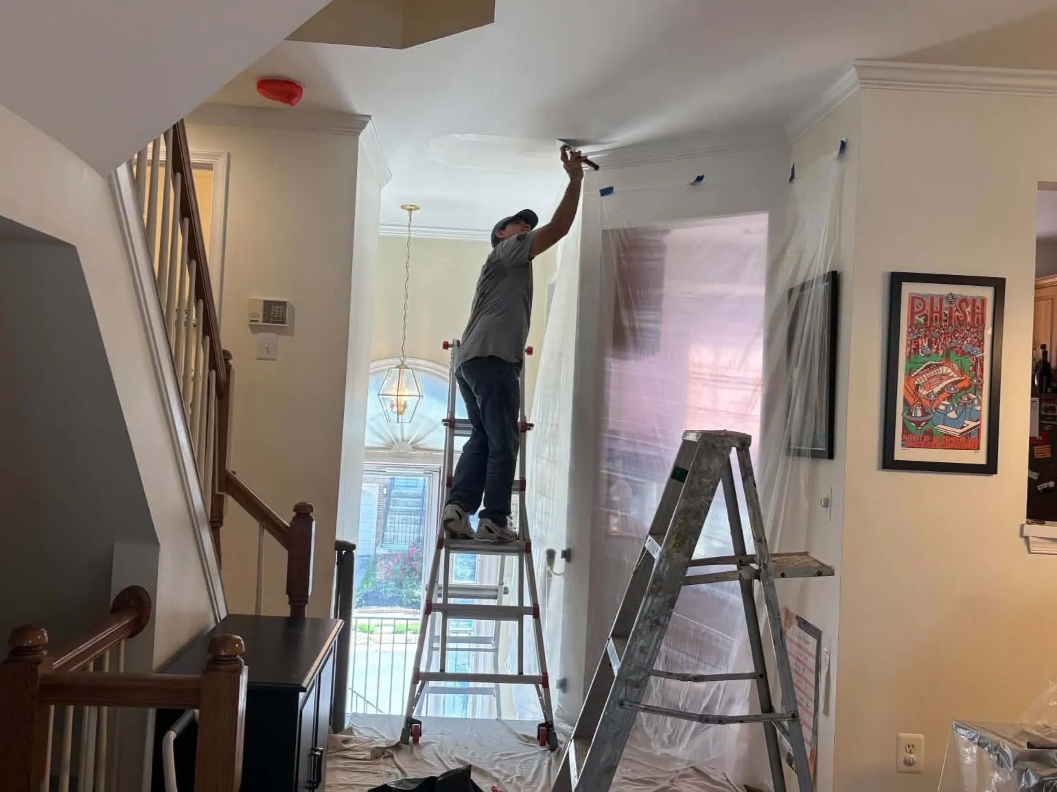 Melvin finishing drywall repairs on a high ceiling using a ladder